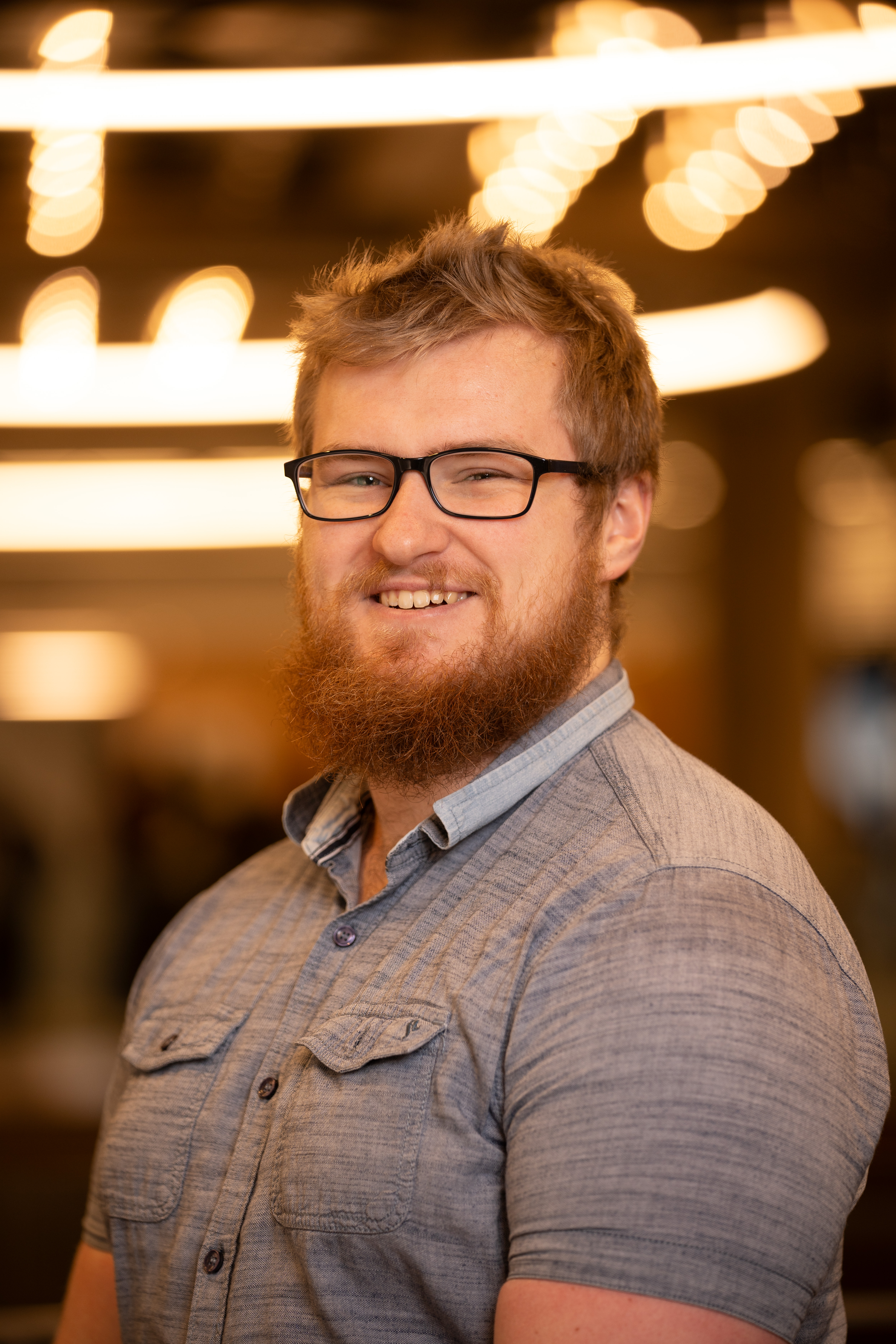 Jeanine White smiling in a red plaid shirt and tortoise shell glasses
